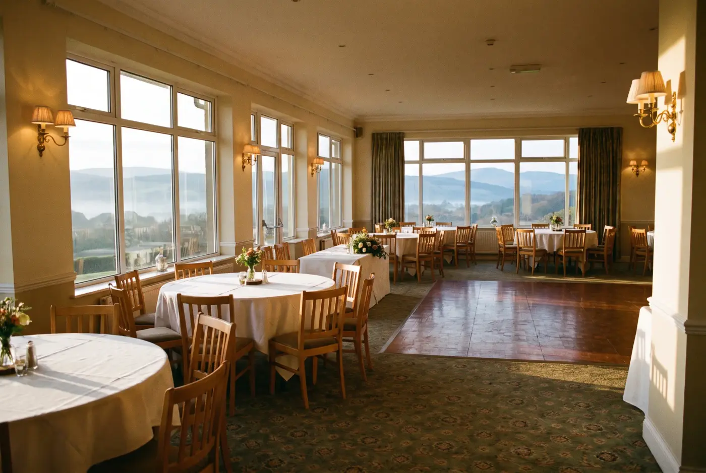 The same room laid for a wedding breakfast: round tables in white linen, flowers, the same valley through the windows